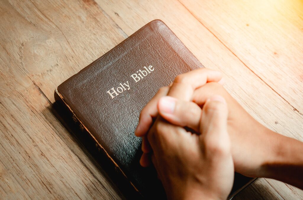 Hands of prayer on a Holy Bible on wood table with window light.christian backgound